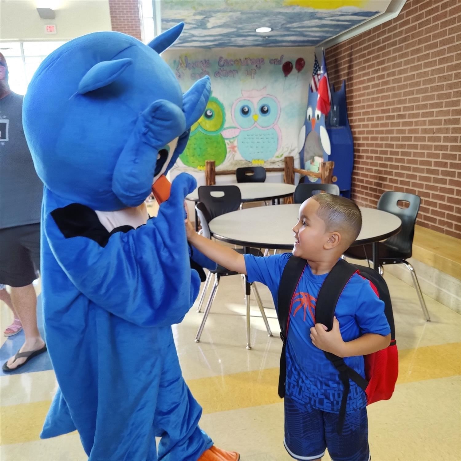 Ollie the Owl high fives a student in the cafeteria